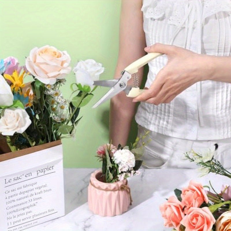 Person arranging flowers with scissors on a table with floral arrangements and a green wall.