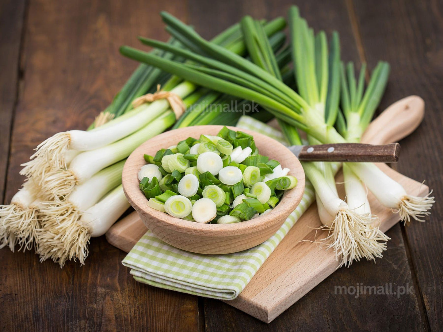 Green onions with a bowl of chopped green onions on a wooden cutting board.