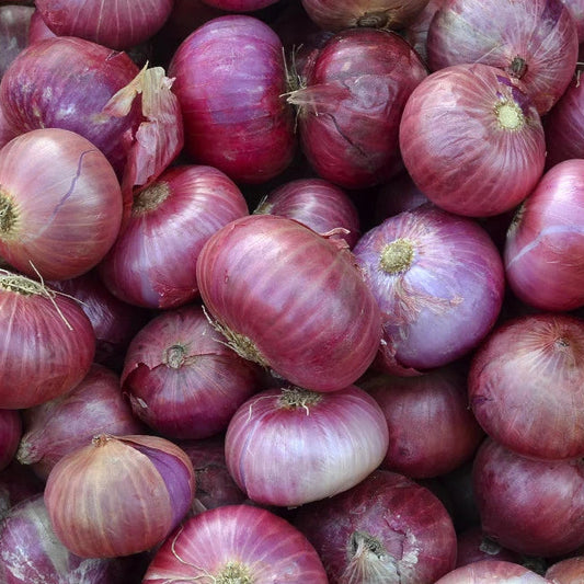 A close-up pile of red onions with purplish-red papery skins and pale off-white bulbs showing through, filling the entire frame.