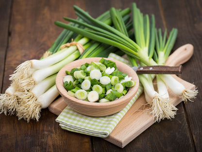 Green onions with a bowl of chopped green onions on a wooden cutting board.